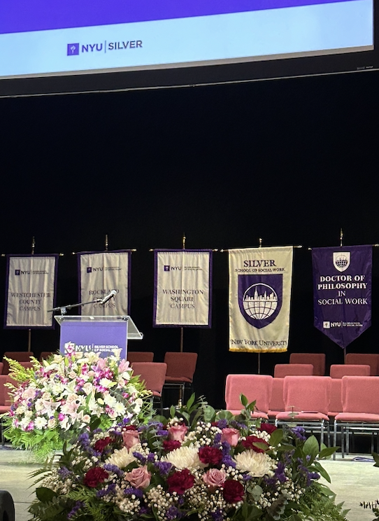 Large bouquets of flowers adorn a stage set for the NYU Silver School of Social Work graduation ceremony.